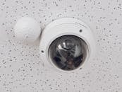 Close-up of a round dome surveillance camera installed on a speckled ceiling for security monitoring.